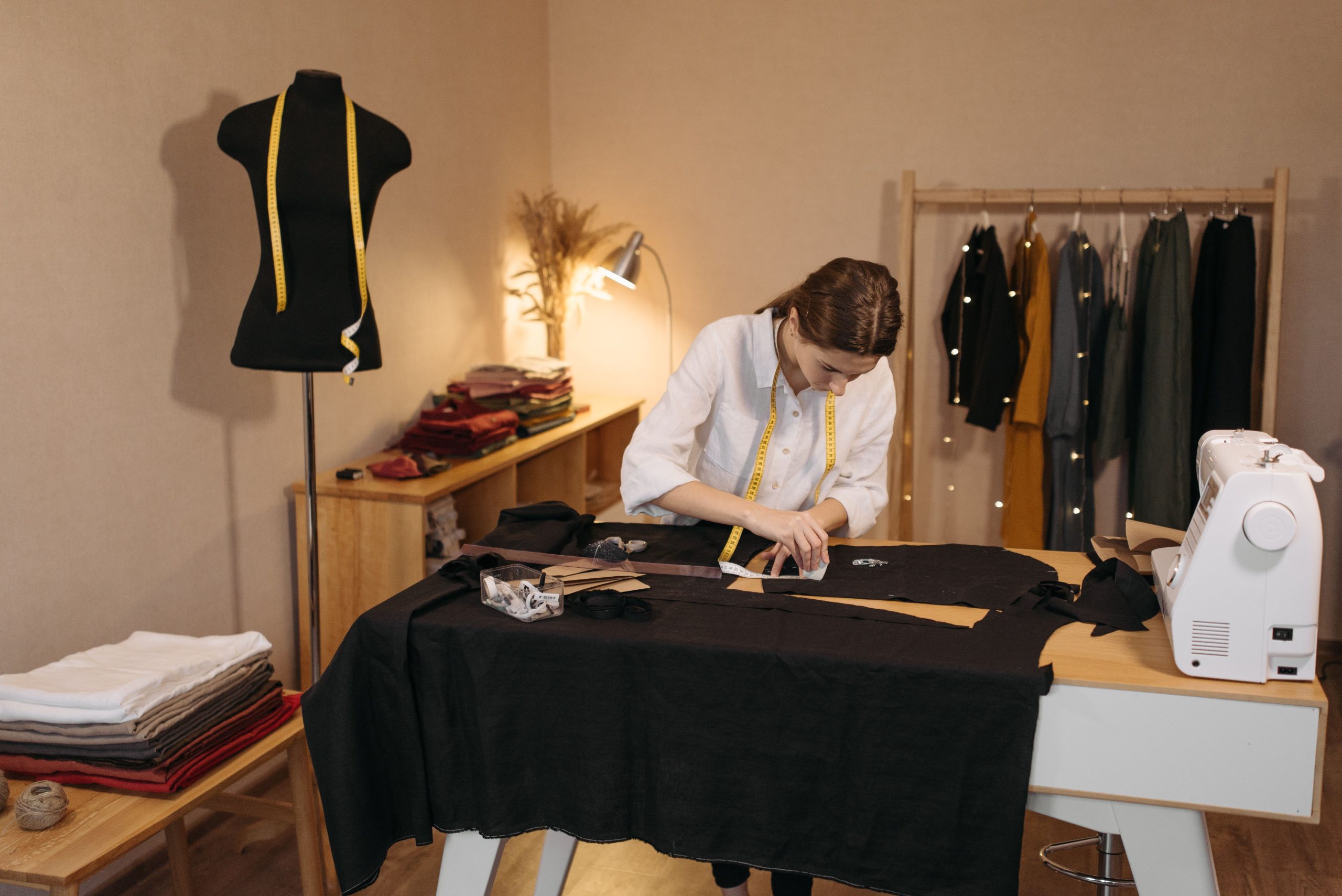 A woman involved in dressmaking tasks in a studio, measuring and cutting fabric.